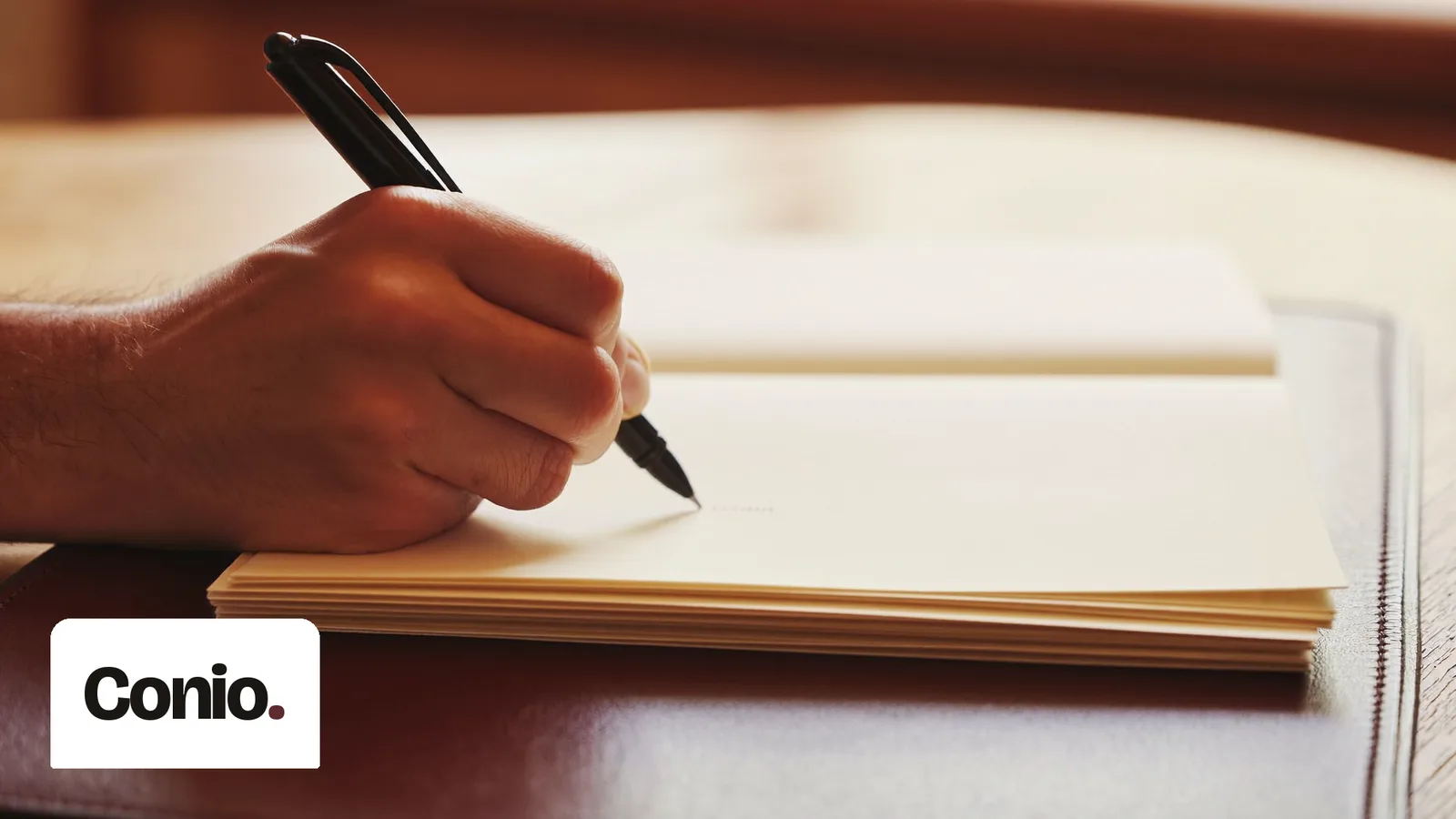 Una mano con la penna firma su fogli color crema, sopra una cartella in pelle scura